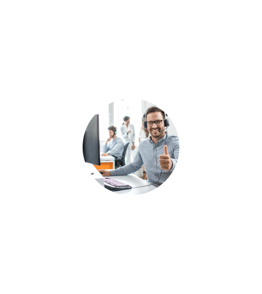 Smiling customer support agent wearing a headset giving a thumbs up at his desk in a busy office.