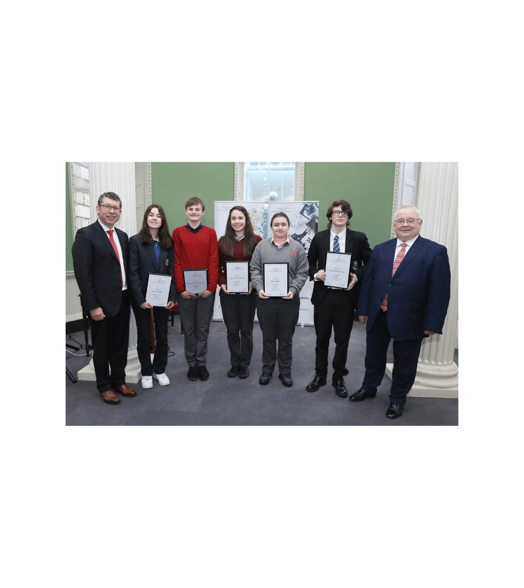 Group of students proudly holding certificates alongside officials at the Oireachtas Essay Competition award ceremony.