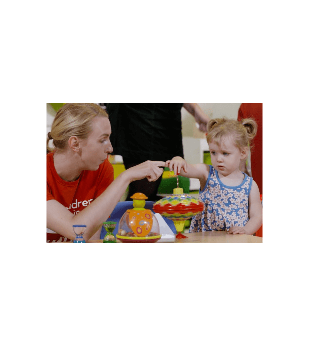 Volunteer from Children in Hospital Ireland engaging a young child in play with colourful toys at a hospital activity table.