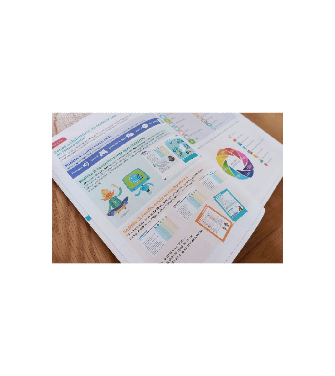 Open Gaeilge Abú! textbook showing colourful illustrations, charts, and Irish language learning activities