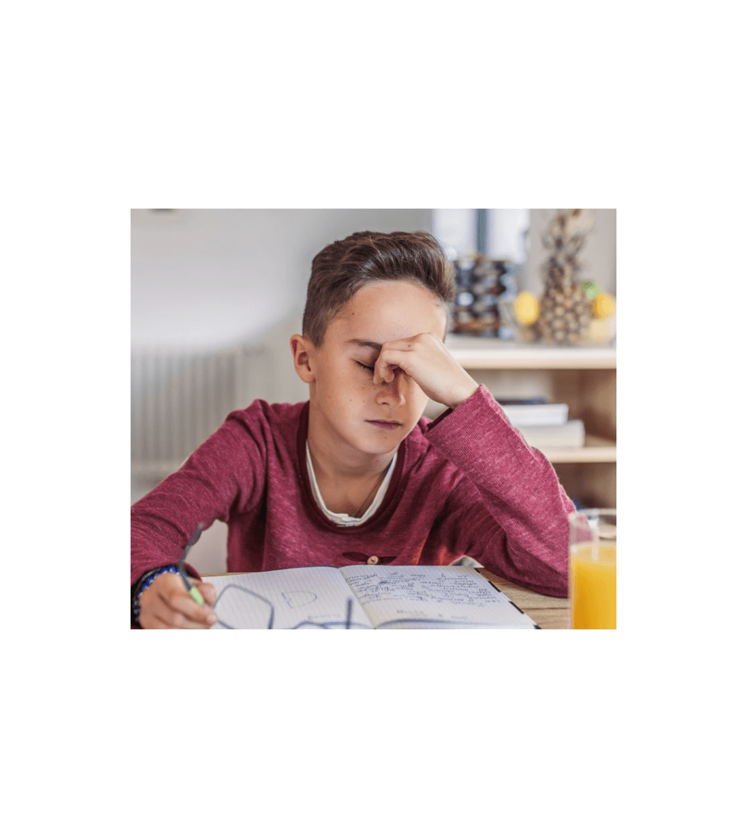 Frustrated student in red shirt rubbing eyes while studying at a desk with an open notebook and a glass of orange juice.