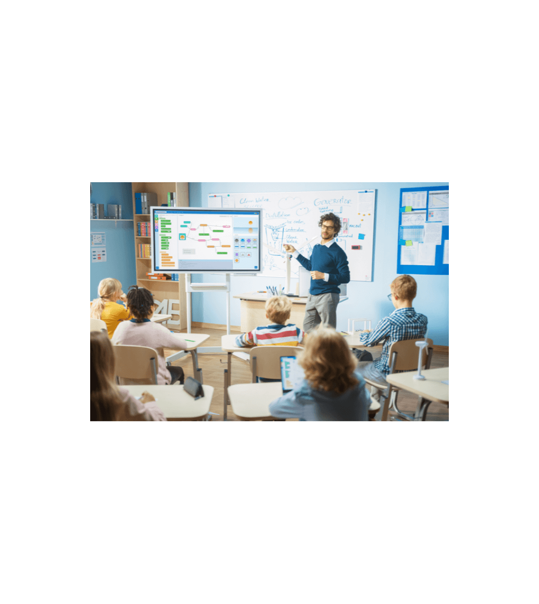 Teacher explaining a digital lesson on a smartboard to engaged primary students using tablets in a modern classroom.