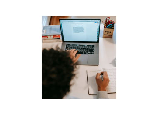 Student typing on a laptop while taking notes in a notebook at a desk